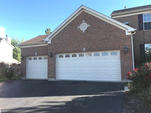 Brick suburban house with two white garage doors and a paved driveway in sunlight