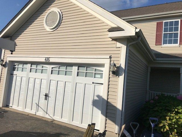 White double garage doors on a beige house exterior with a small circular attic vent above.