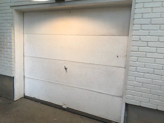 White garage door set in a brick building wall with a small latch near the bottom.
