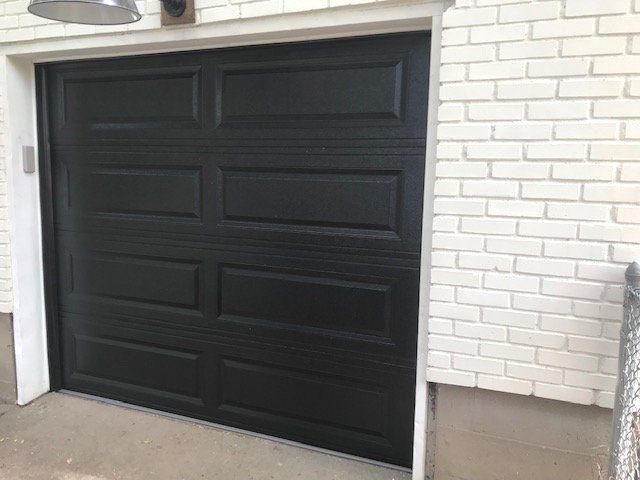 Black garage door set in a white brick exterior wall with a concrete driveway.