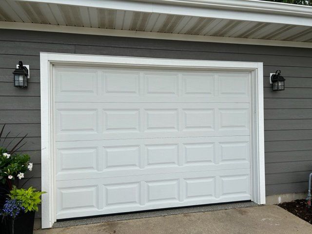 White paneled garage door with two black wall lanterns on a gray house exterior