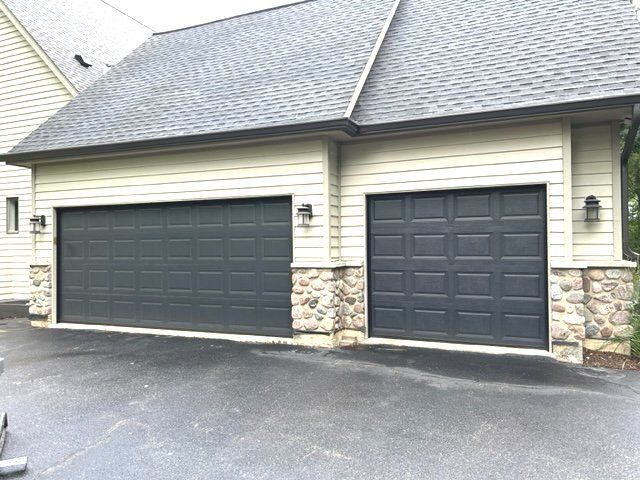 Two dark garage doors on a beige house with stone accents and a paved driveway