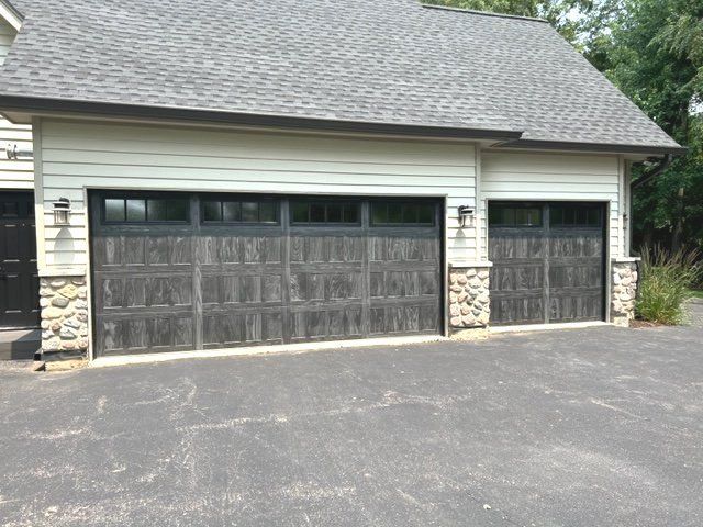 Two-car garage with dark wood doors and white siding beside a paved driveway