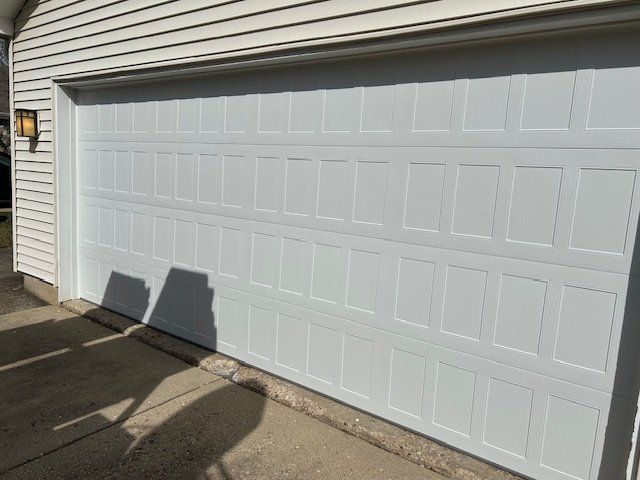 White two-car garage door on a house exterior, with sunlight casting shadows on the pavement.
