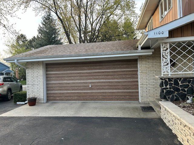 Suburban house driveway with closed brown garage door and brick exterior.