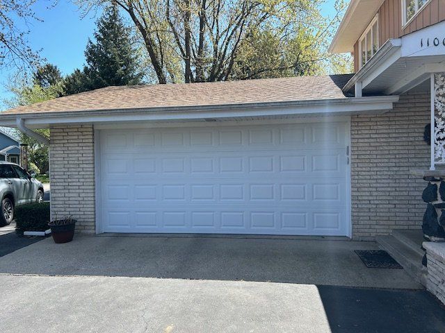 White two-car garage with a closed door and driveway under a brick house exterior.