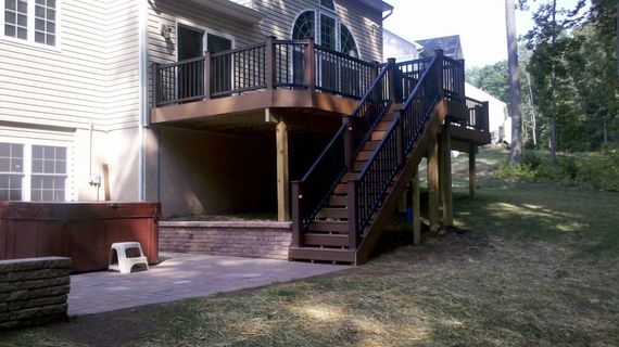 A wooden deck with stairs attached to a two-story home, hot tub on the patio.