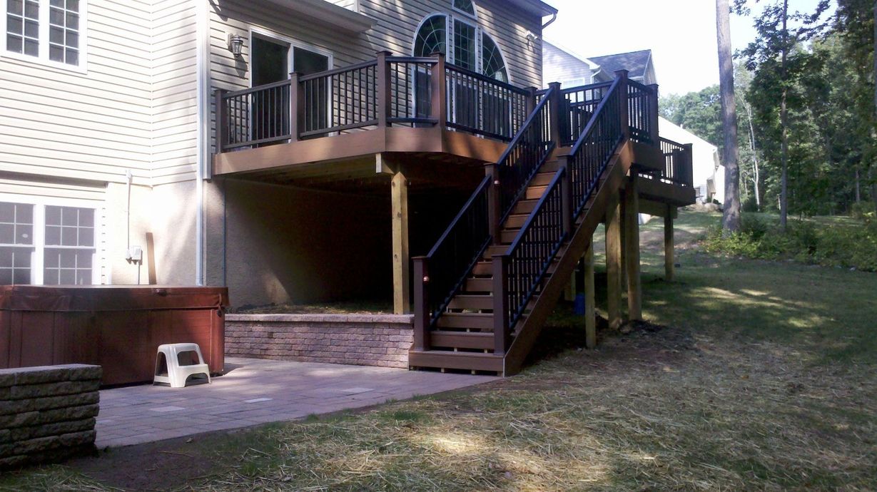 A wooden deck with stairs attached to a two-story home, hot tub on the patio.