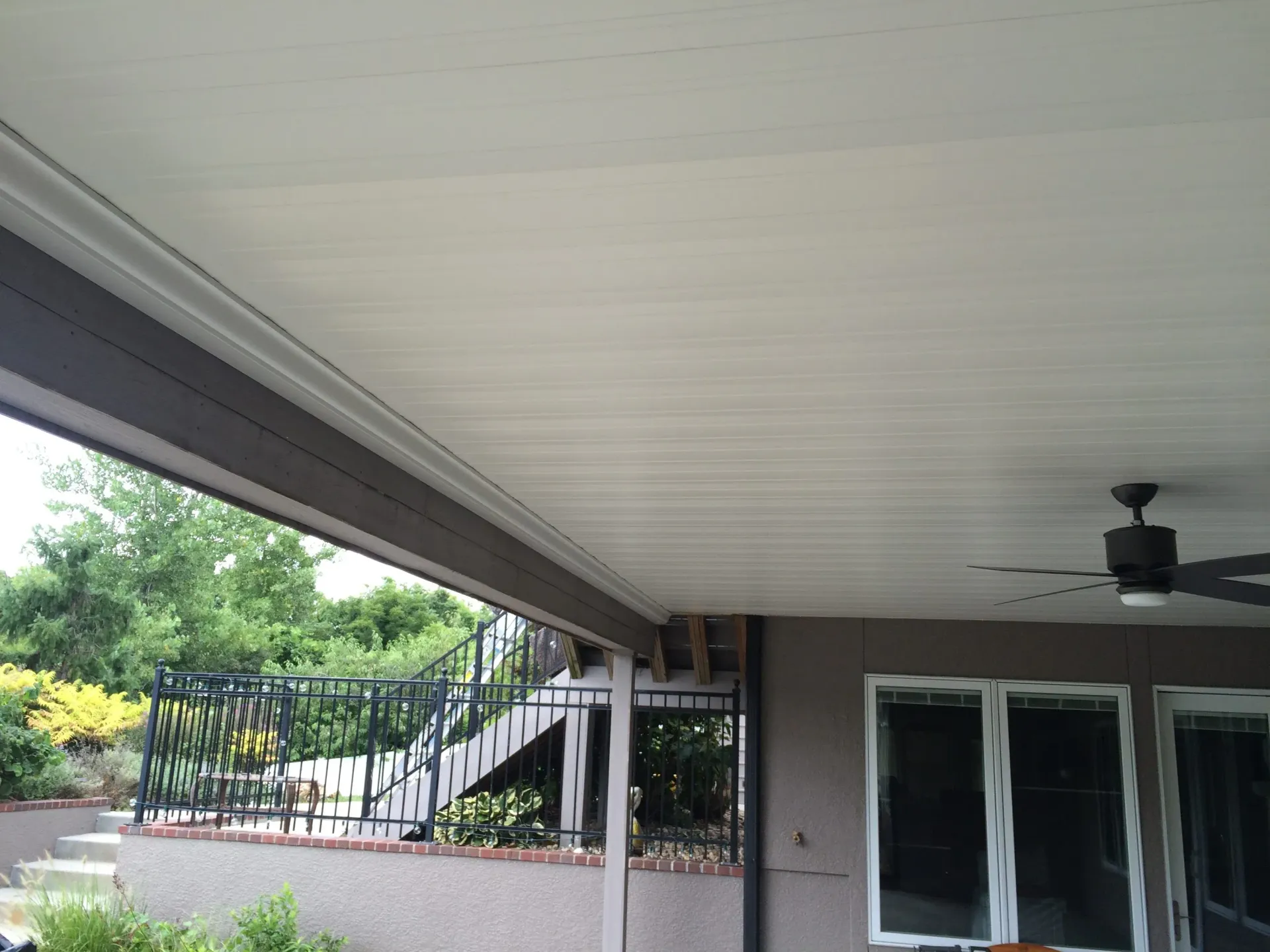 Covered patio with ceiling fan, overlooking a yard and steps.