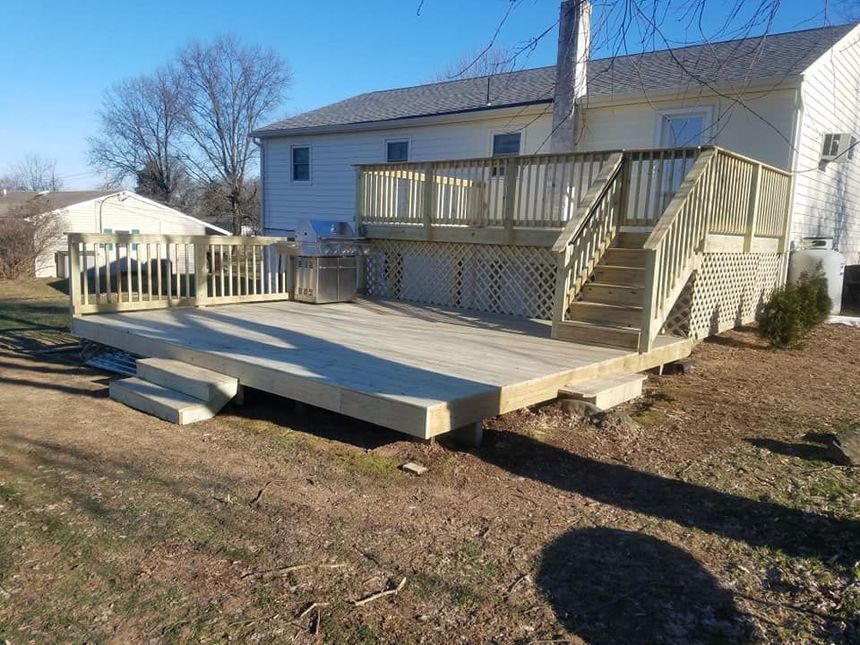 Newly built wooden deck with stairs in backyard, near a house on a sunny day.