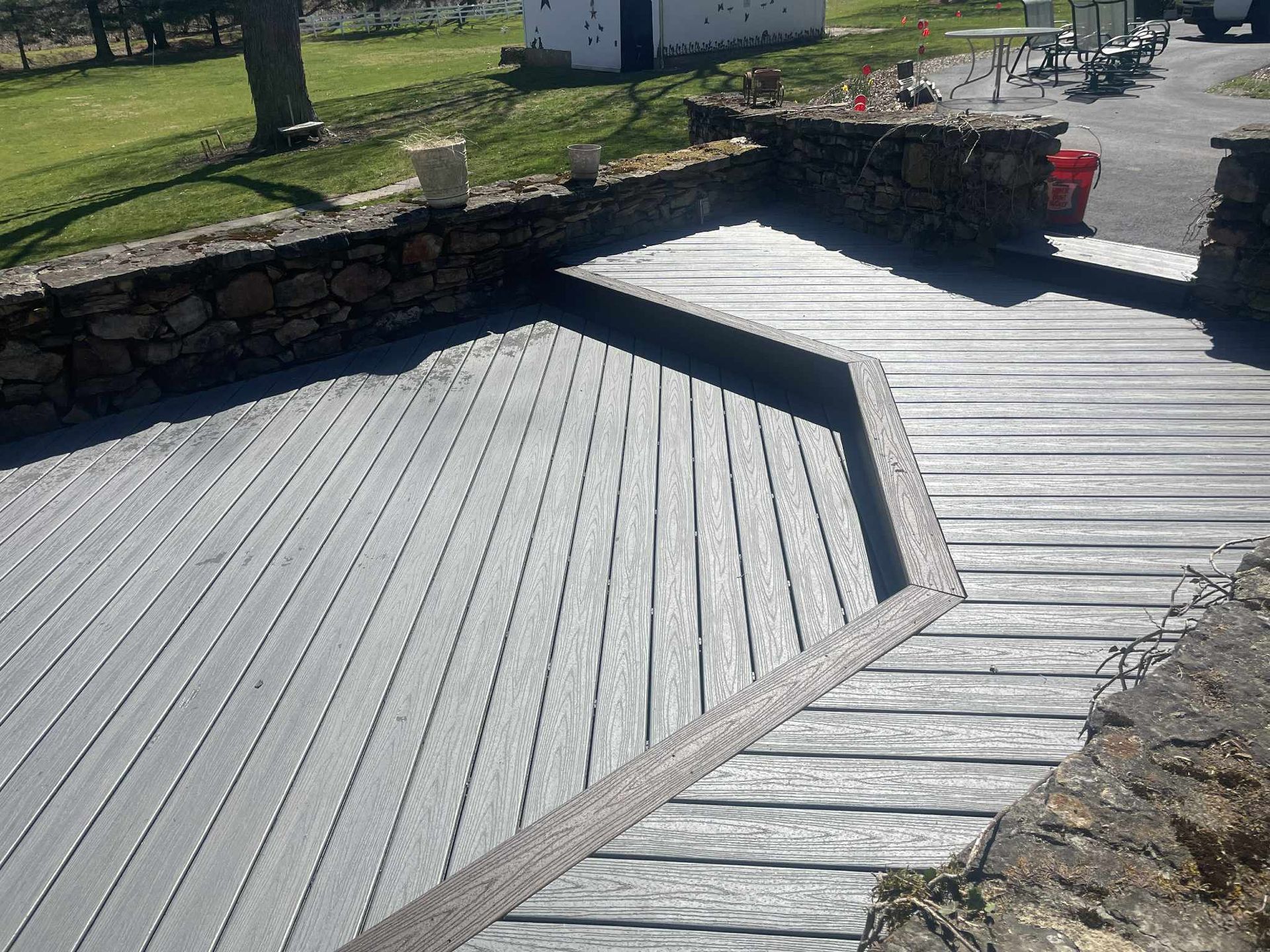 Outdoor wooden deck with stone retaining walls. Gray wood planks, angled design.