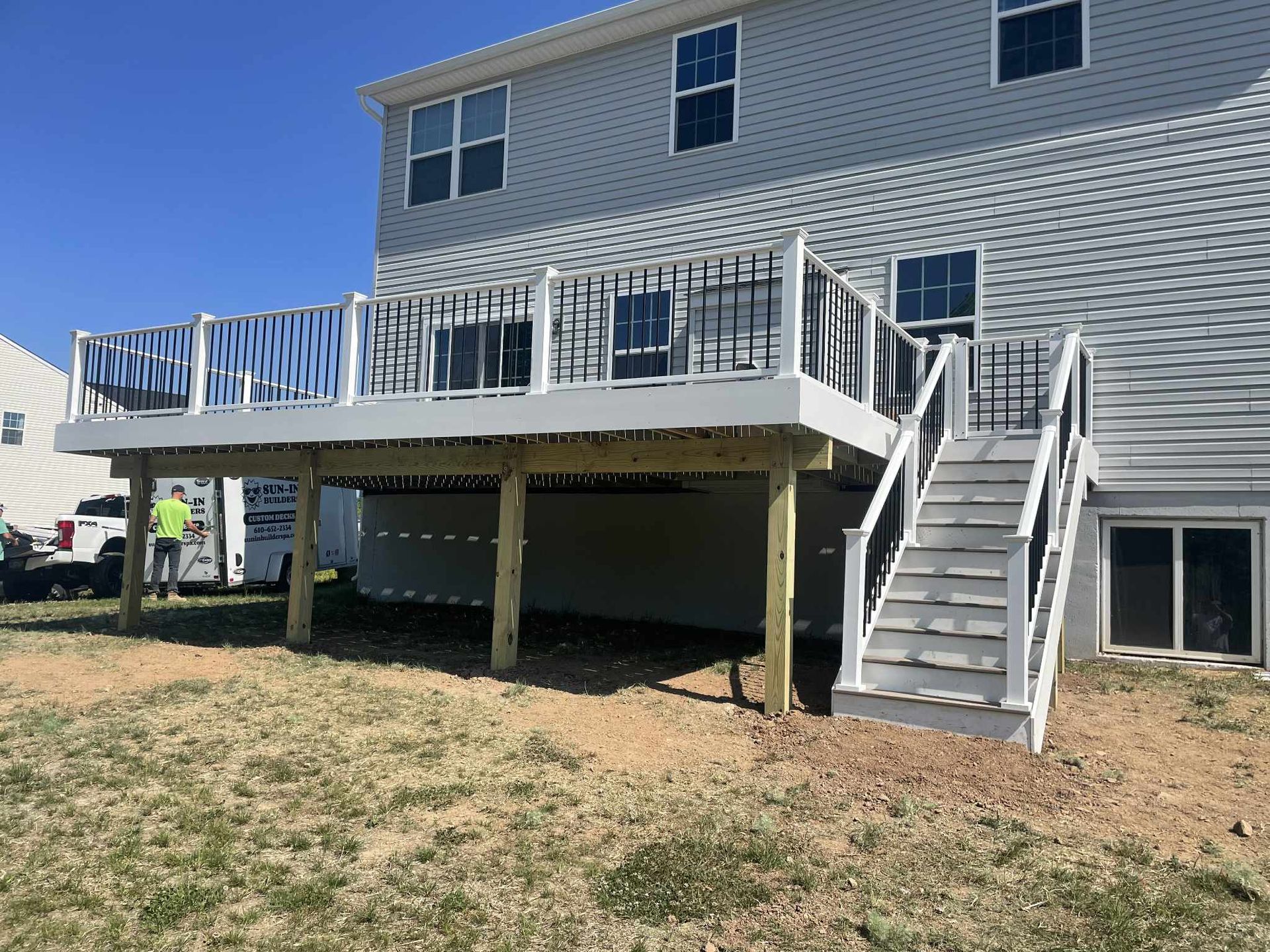 A newly built gray deck with black railings and stairs attached to a two-story gray house.