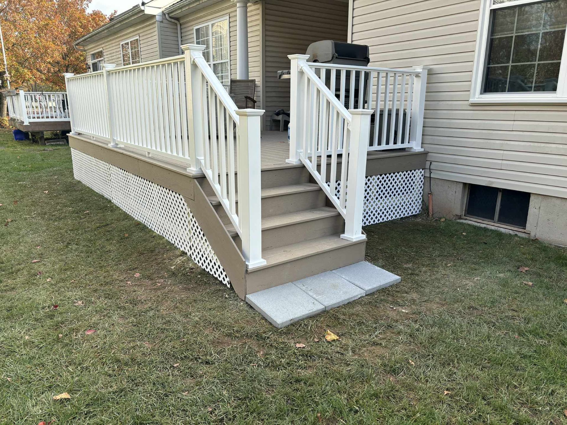 Deck with white railing and steps leading to a yard, tan skirting, and a grill.