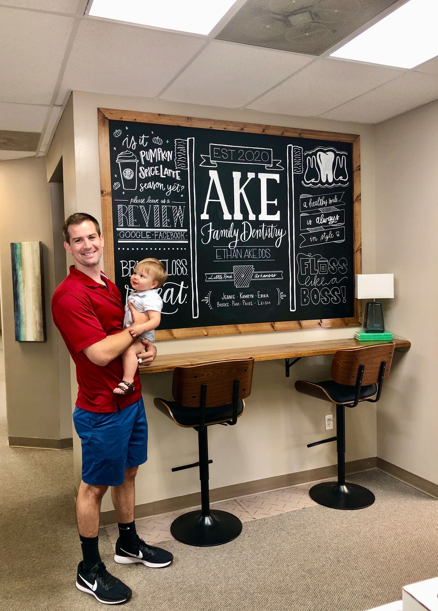 a man is holding a baby in front of a chalkboard .