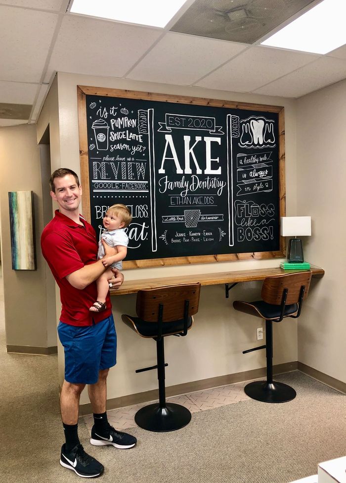 a man is holding a baby in front of a chalkboard .