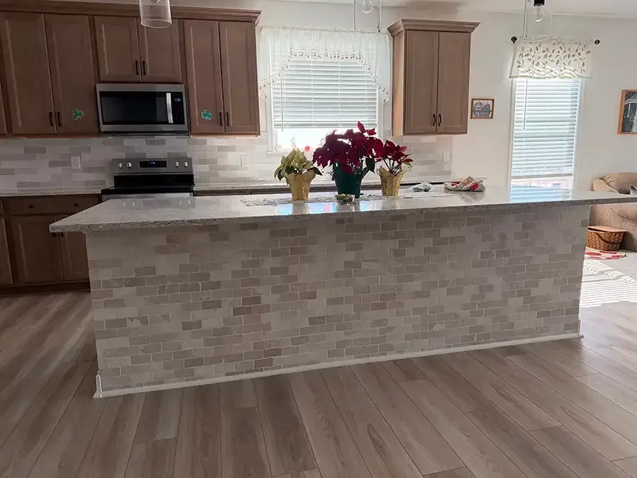 A modern kitchen featuring off-white subway tile walls, a tea kettle, framed botanical prints, and glassware on shelves.