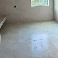 Empty bedroom with beige carpet and walls, vaulted ceiling, arched window, and open doorway leading to a wooden hallway.
