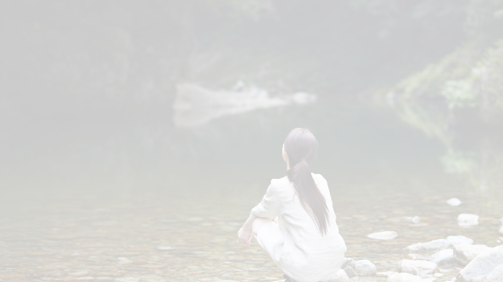 Woman in white by a calm lake, looking at the water.