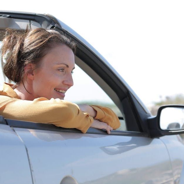 Eine Fahrlehrerin lehnt sich aus dem Fenster eines silbernen Autos.