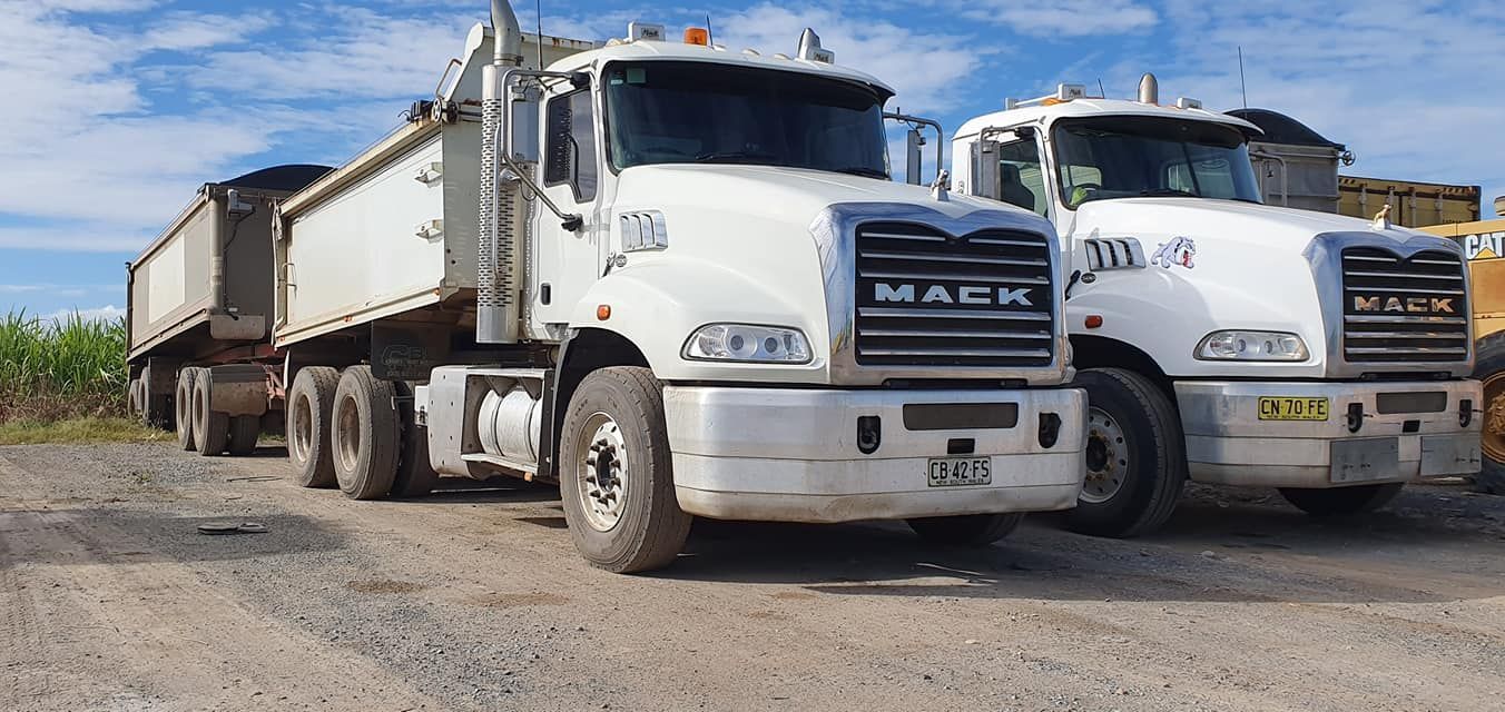 Two white Mack dump trucks parked on a gravel lot under a clear sky — Compass Equipment Hire in Brunswick Heads, NSW