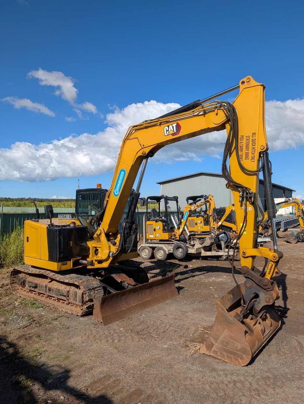 Yellow excavator on a dirt lot under a blue sky, with other construction equipment in the background — Compass Equipment Hire in Alstonville, NSW