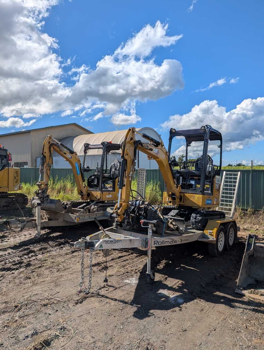 Two yellow mini excavators on a flatbed trailer in a gravel yard under a blue sky — Compass Equipment Hire in Kyogle, NSW