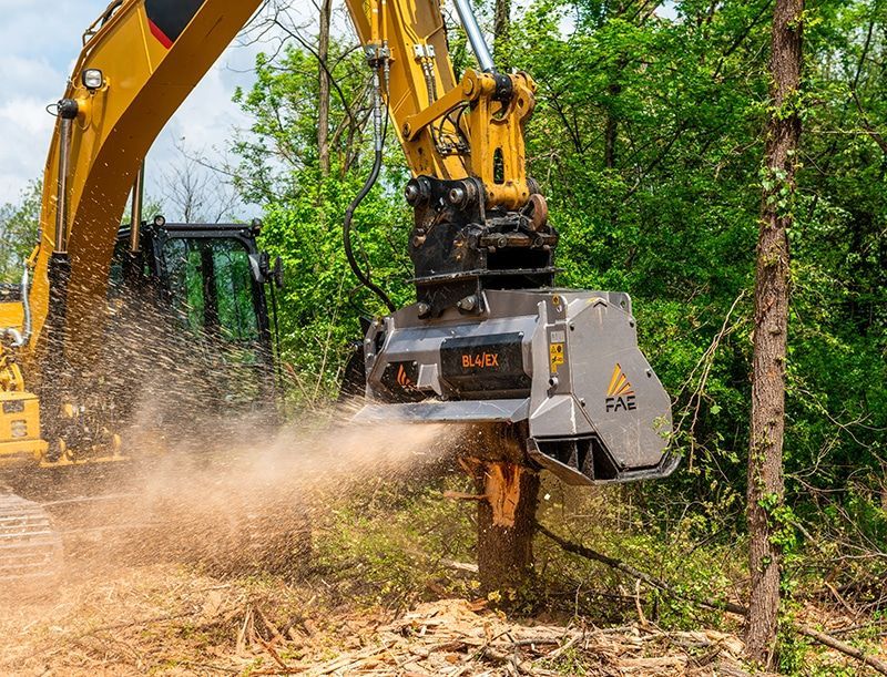 Yellow excavator cutting brush in a wooded area, kicking up dust and debris — Compass Equipment Hire in the Northern Rivers, NSW
