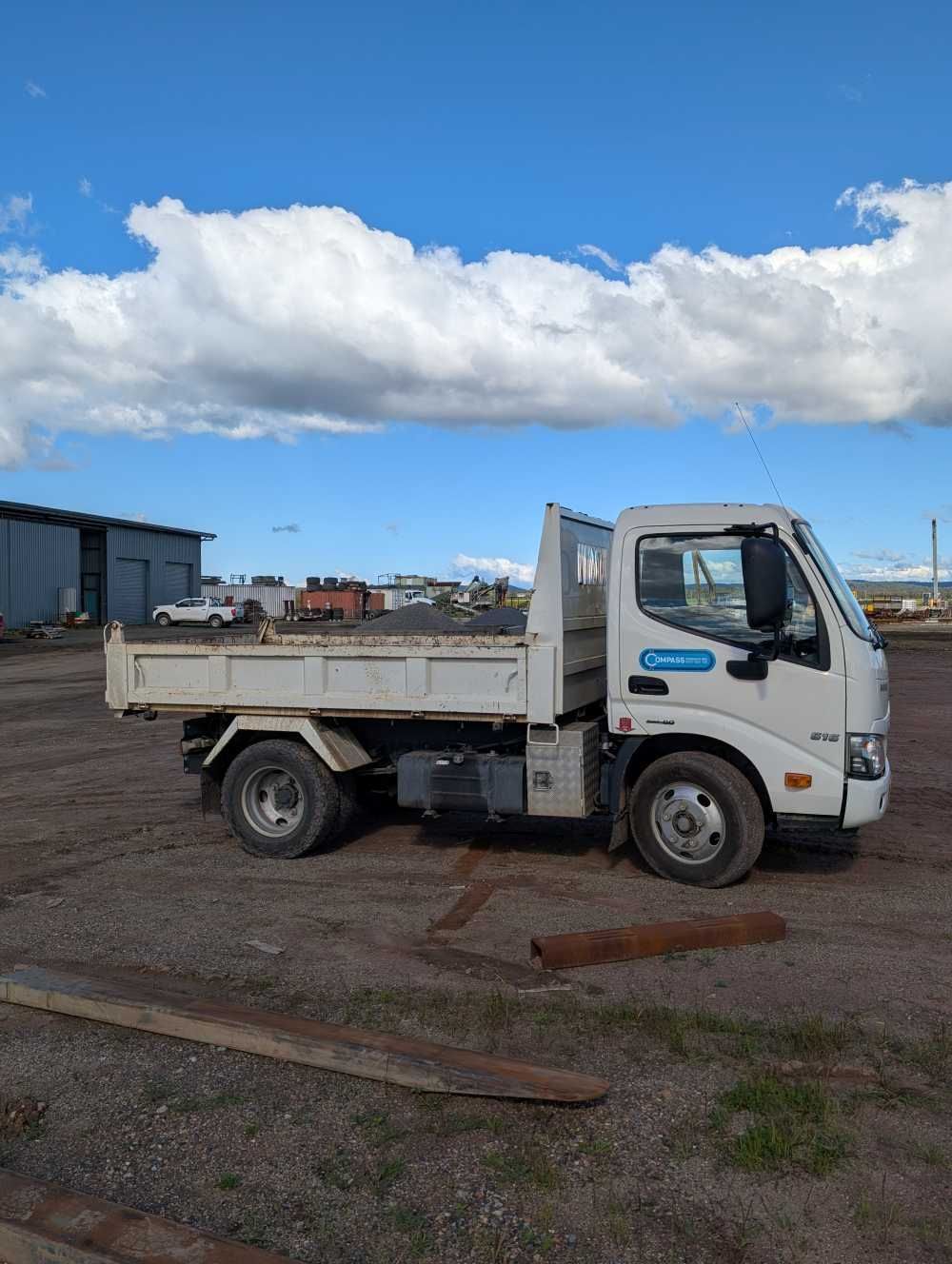 White flatbed truck parked on a dirt lot under a cloudy blue sky — Compass Equipment Hire in Alstonville, NSW