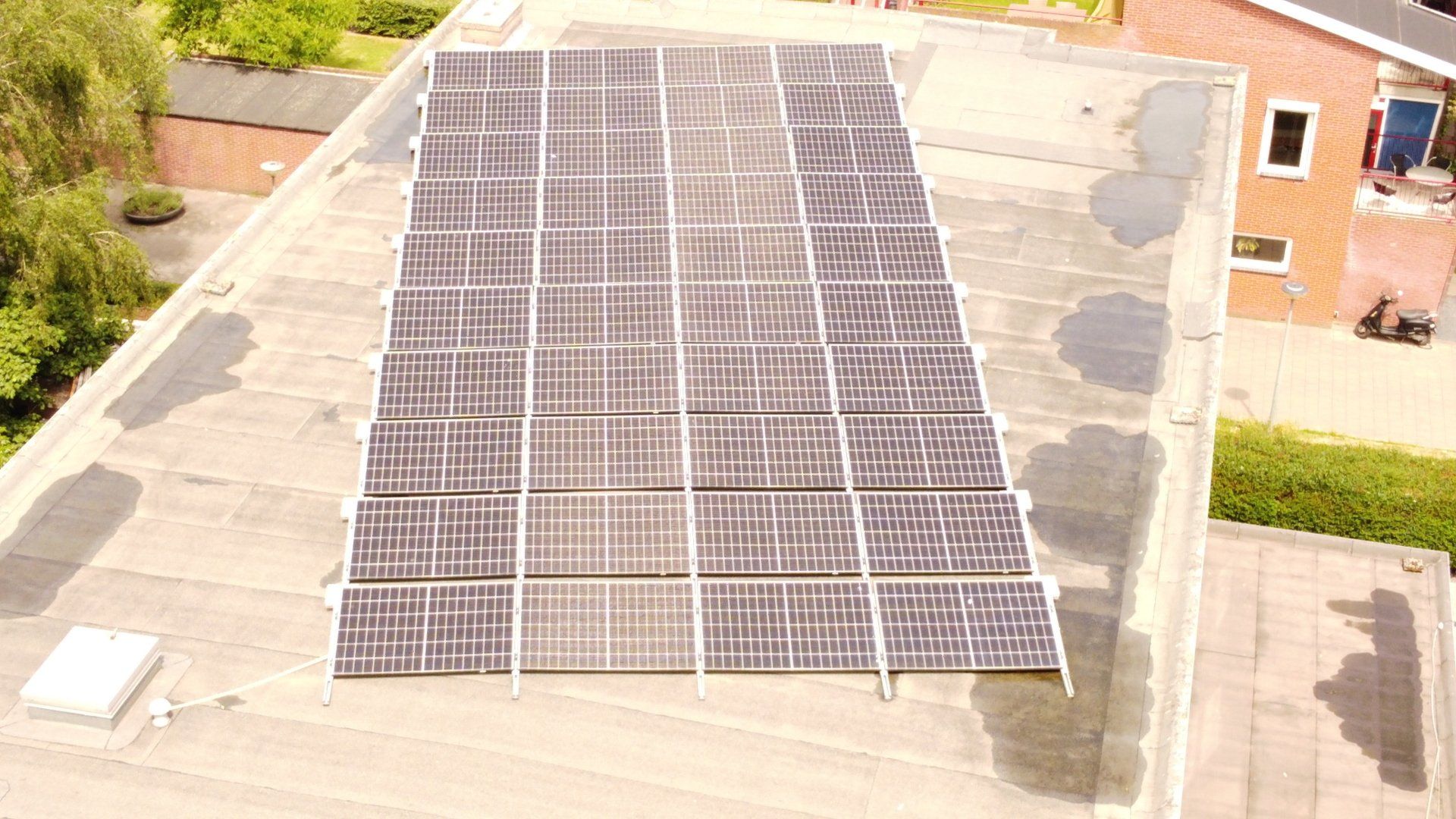 Zonnepanelen op het dak, in rijen gerangschikt, op een lichtgrijs dak naast aangrenzende huizen.
