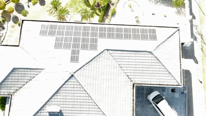Luchtfoto van een huisdak met zonnepanelen en een geparkeerde auto op de oprit.