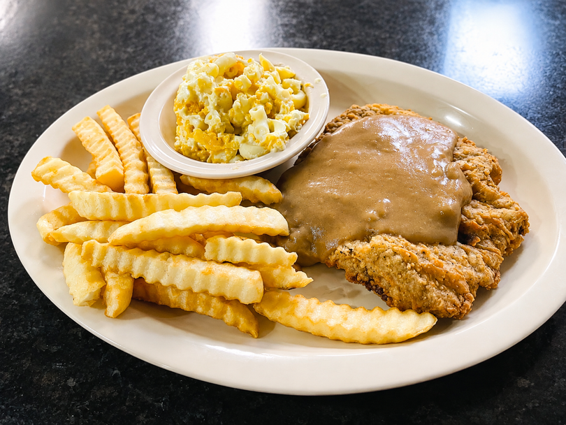 Plate with fried chicken, crinkle-cut fries, and a small bowl of coleslaw on a black table