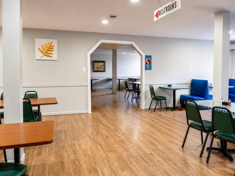 Empty café-style room with wooden floor, tables, chairs, and wall art under bright overhead lights