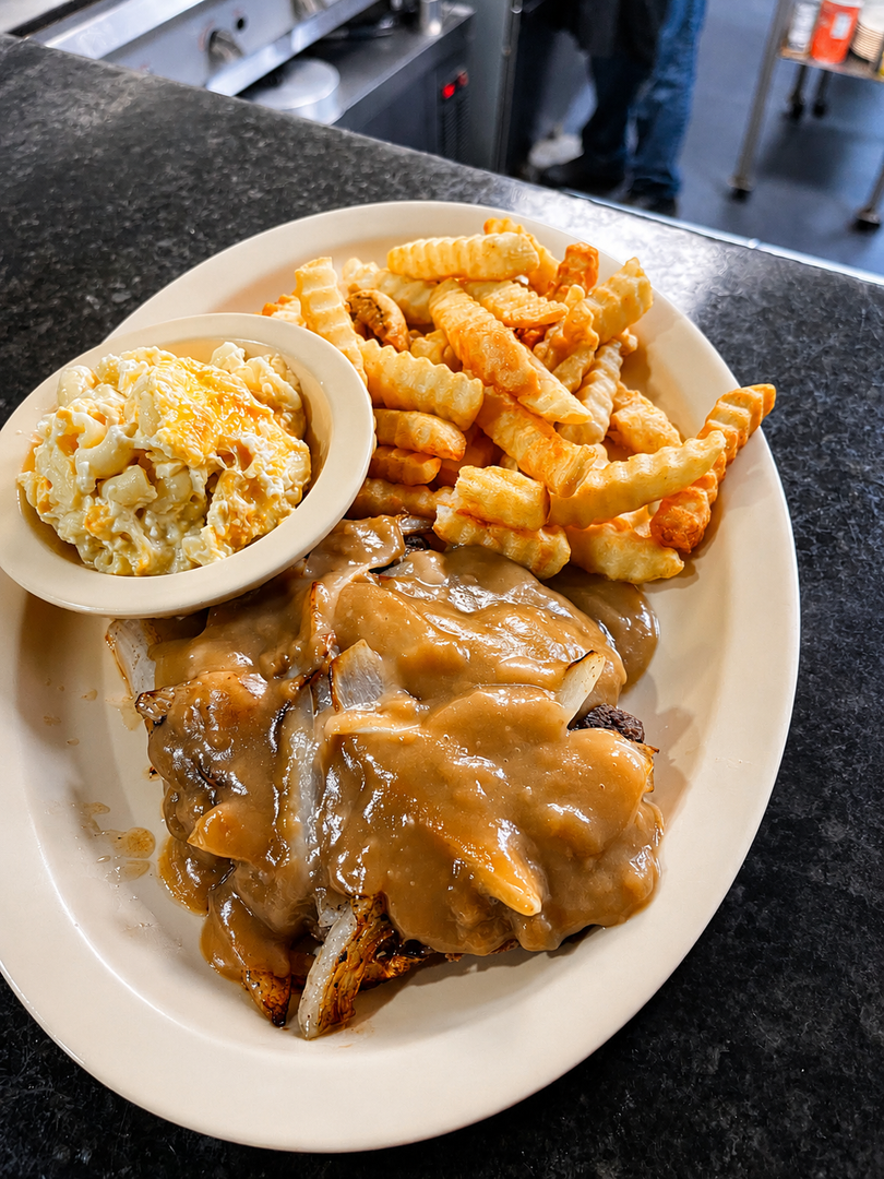 Plate of meat smothered in gravy with crinkle-cut fries and a side of coleslaw on a cafeteria tray