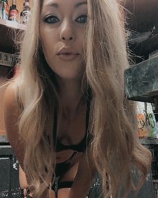 Blonde woman in lingerie, puckering lips. Indoors, low light.