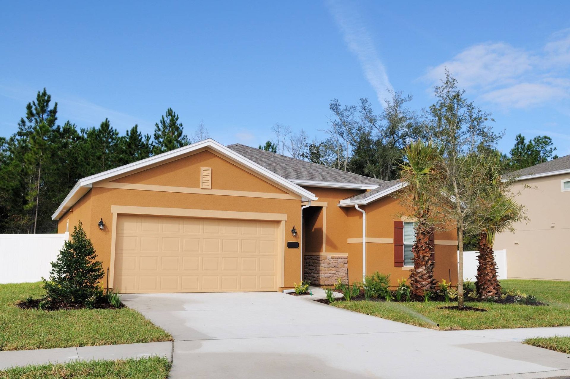 Single-story orange house with a two-car garage, driveway, and green lawn under a blue sky
