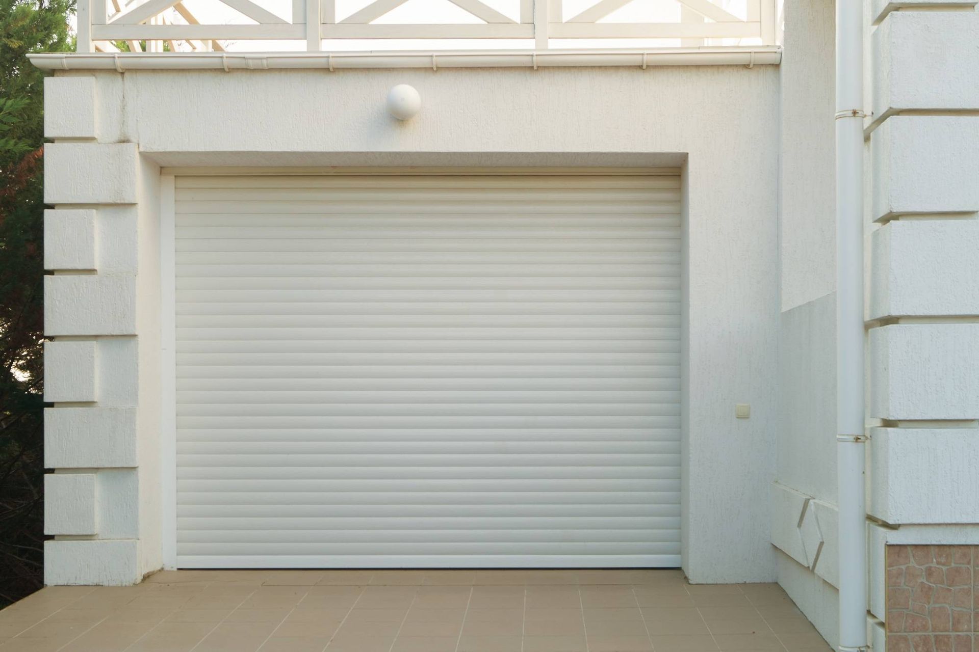 Closed white roll-up garage door with a small round light above it at a building entrance