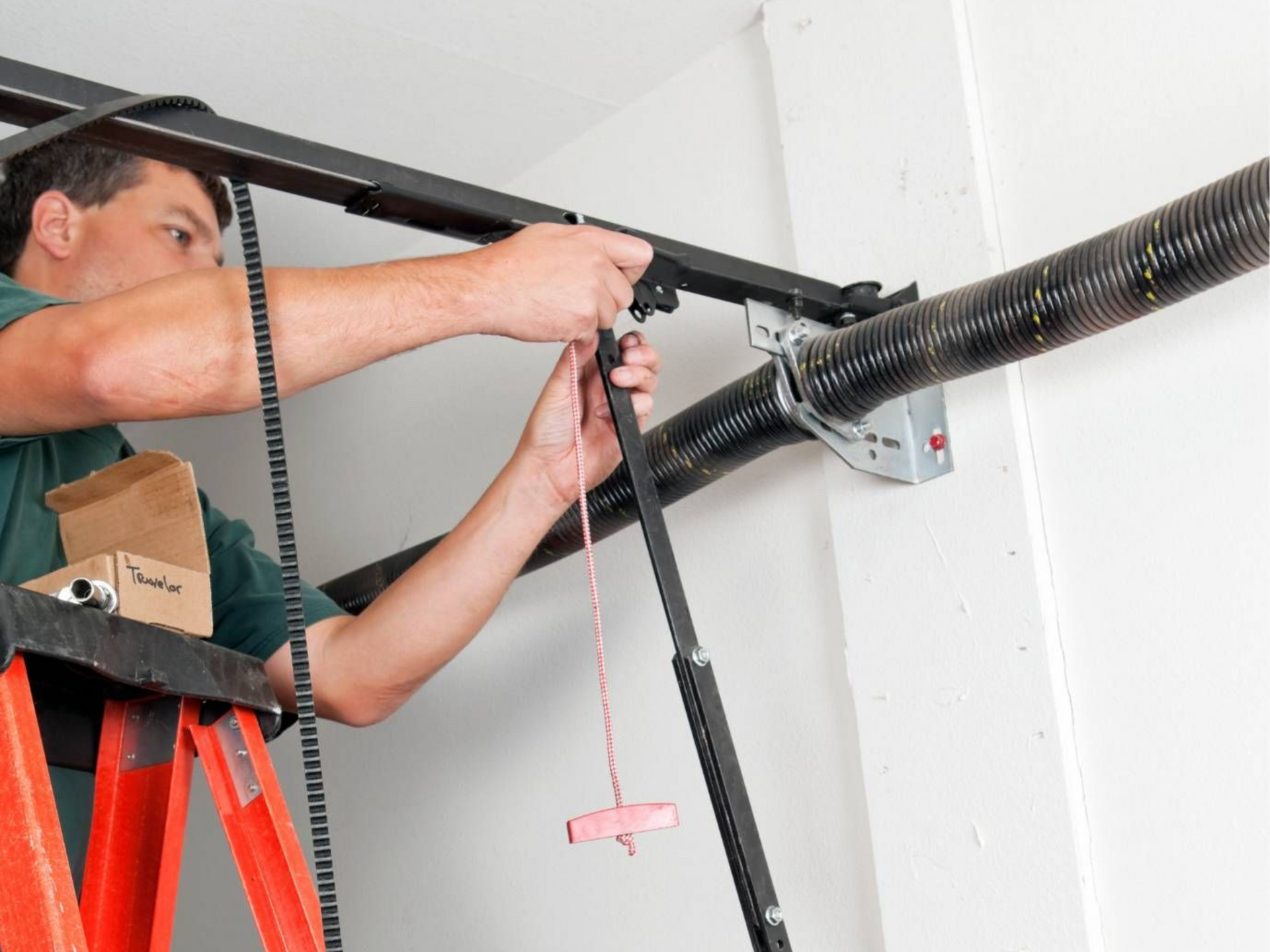 Man installing a garage door opener on a ceiling rail with tools and wiring visible
