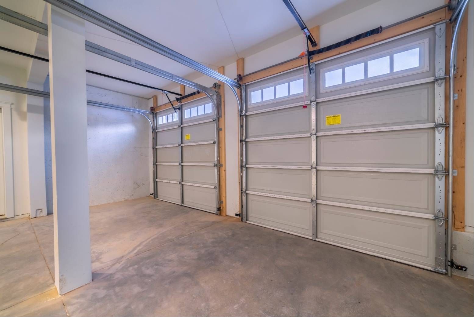 Empty garage interior with two gray paneled doors and a concrete floor under exposed beams.