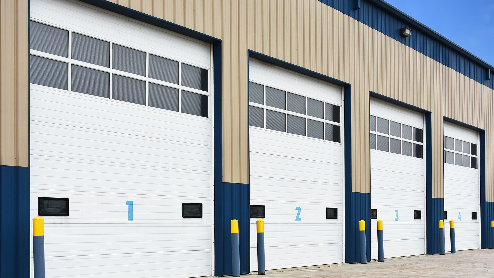 Row of white warehouse loading bay doors on a blue and tan industrial building