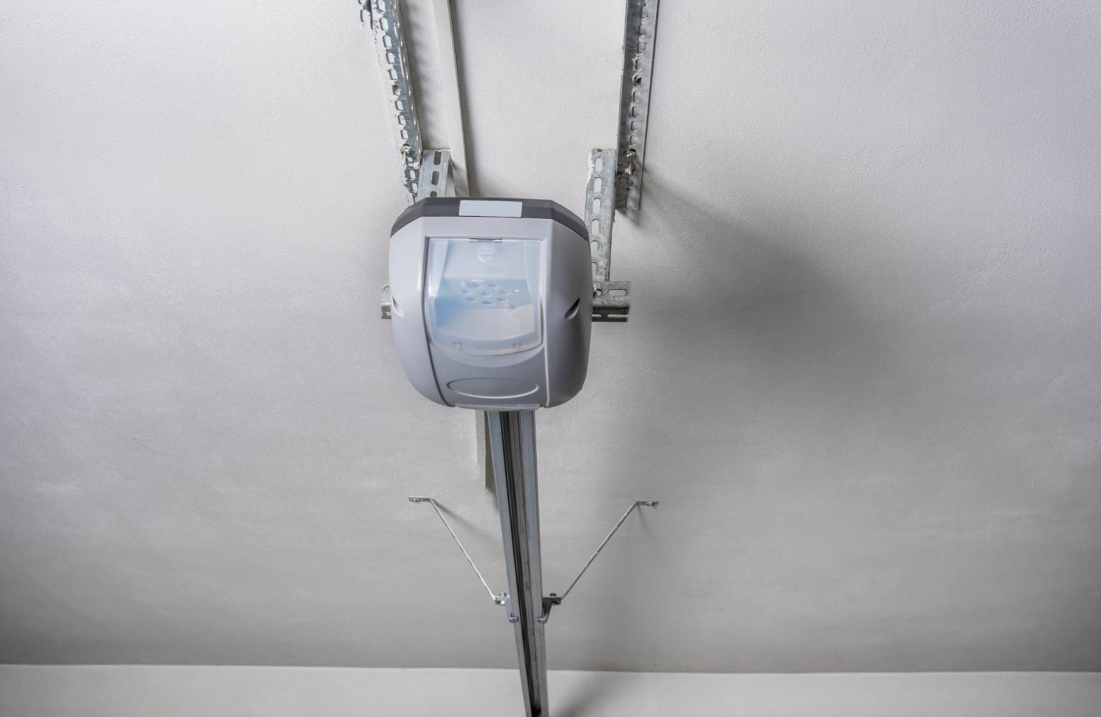 Ceiling-mounted garage door opener with exposed metal rail and wiring on a white ceiling