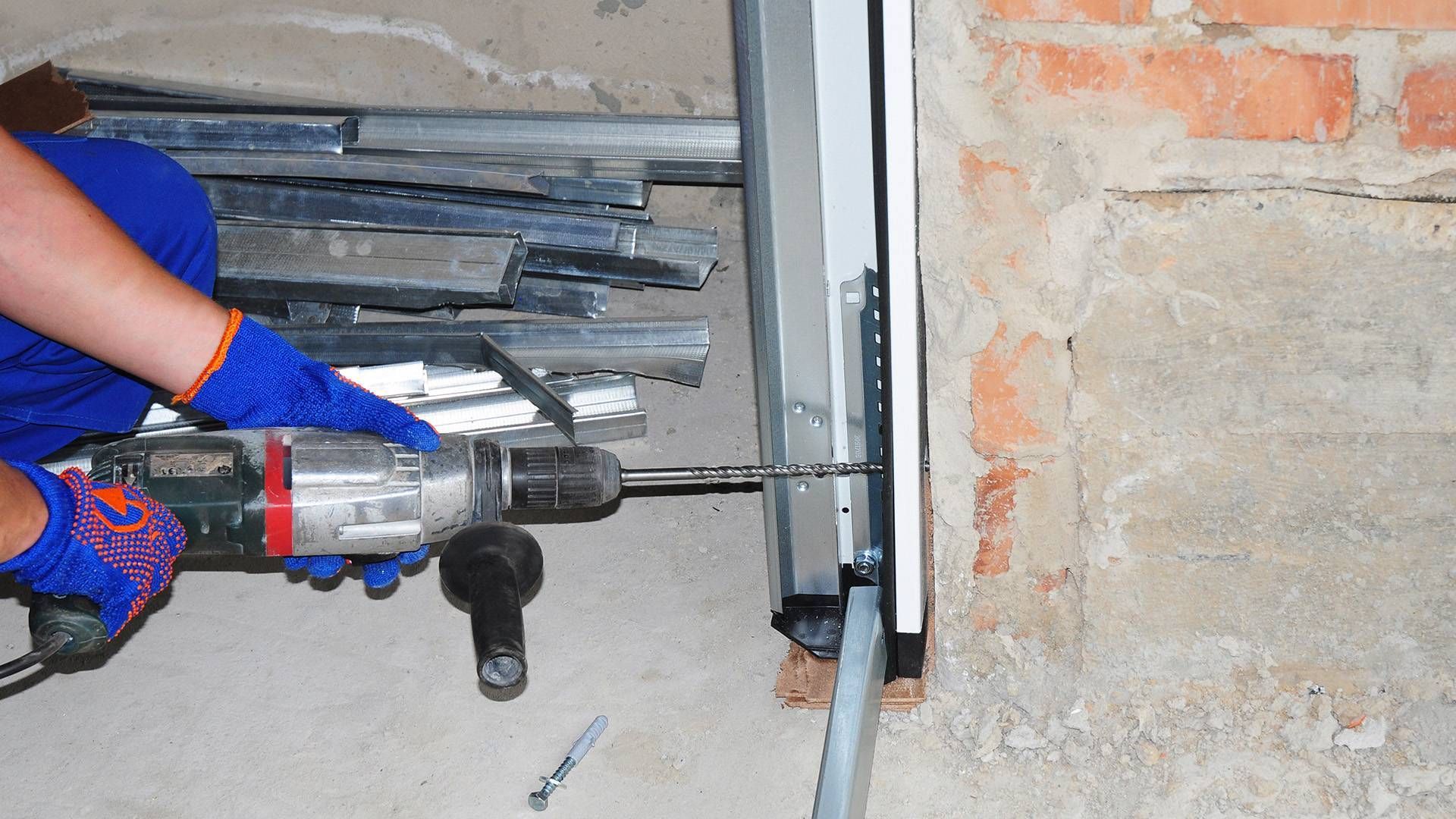 Worker using a power drill on a wall-mounted metal bracket indoors