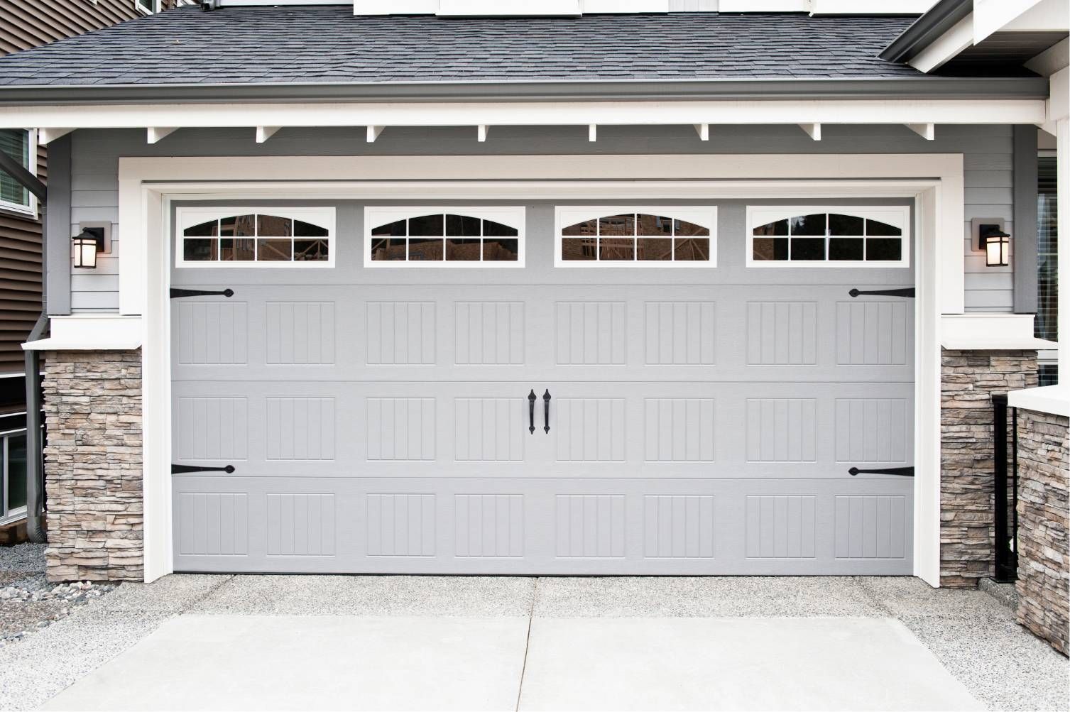 Light gray double garage door with arched windows on a stone-trimmed suburban home.