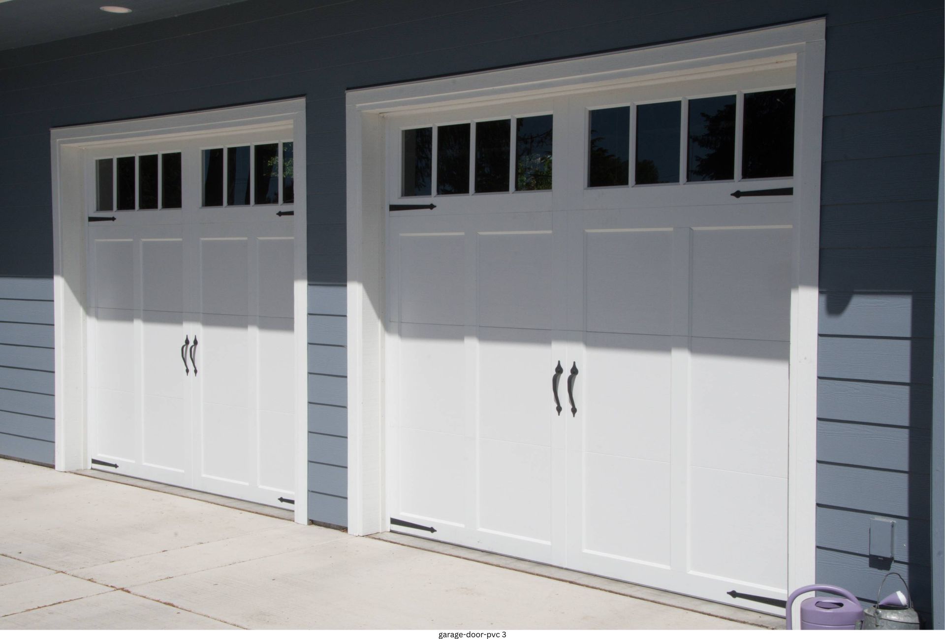 Two white garage doors on a gray house exterior with small upper windows.