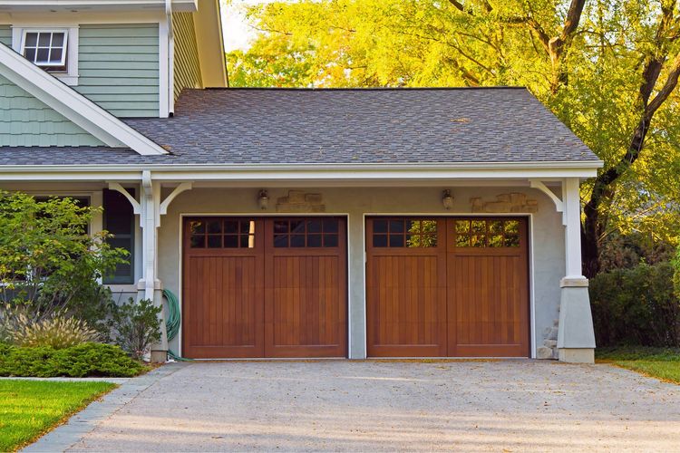Two-car wooden garage doors on a house with white trim and a gravel driveway
