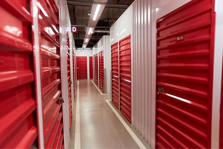 Aisle between red storage unit doors in a brightly lit indoor facility.