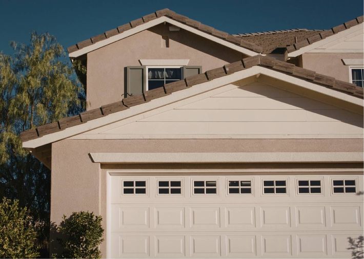 Beige suburban house with a white garage door and a small upper balcony under a clear sky