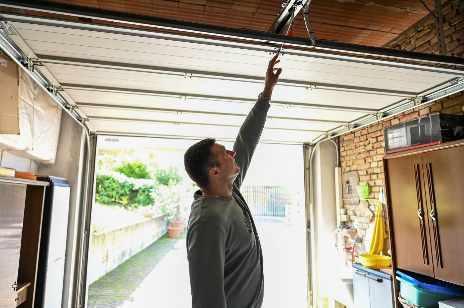 Person reaching up to adjust a garage door track in a cluttered garage interior.