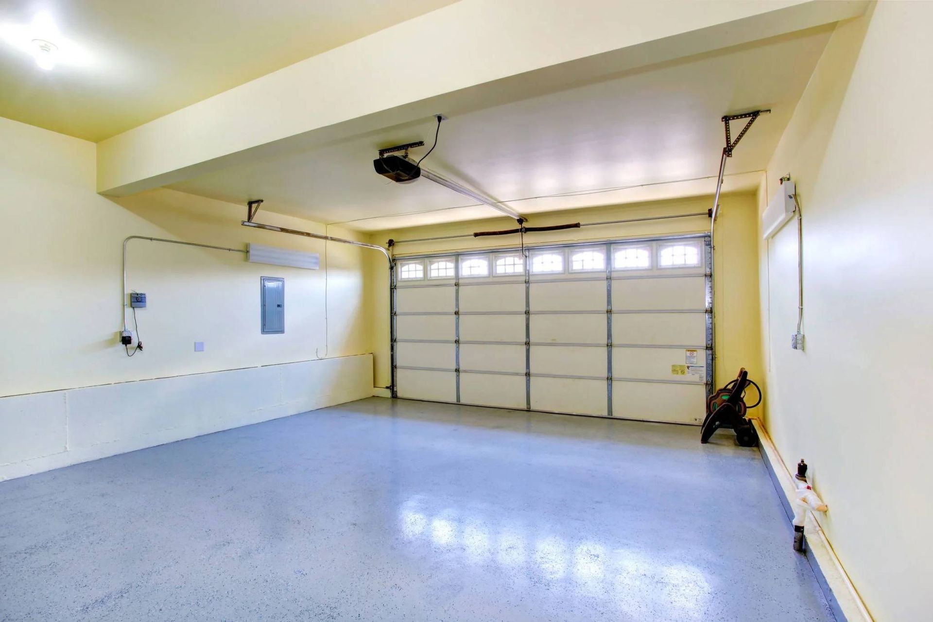 Empty residential garage with a closed white door and light yellow walls, blue epoxy floor, and overhead opener