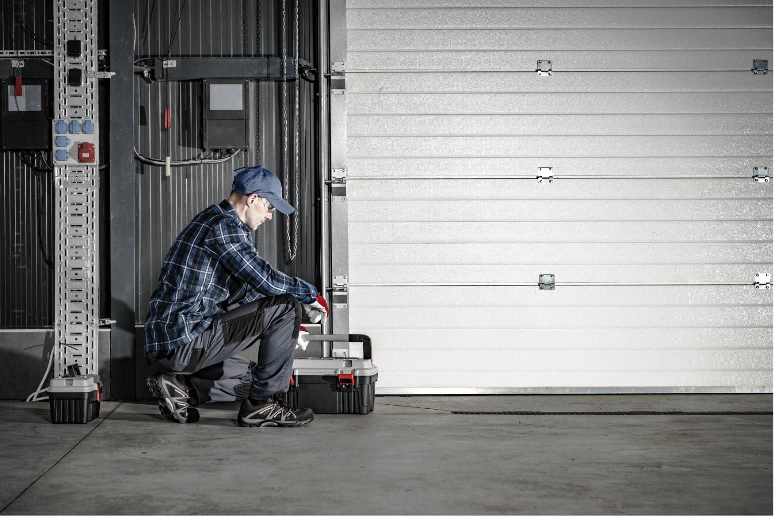 Worker crouching beside industrial equipment in front of a large white garage door