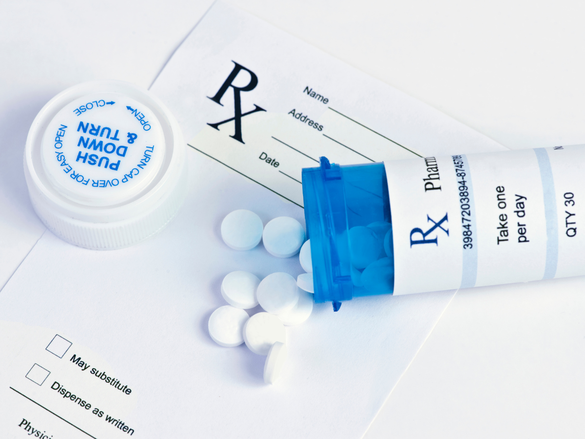 Prescription pill bottle, spilled white tablets, and blue-capped medicine tube on a white background